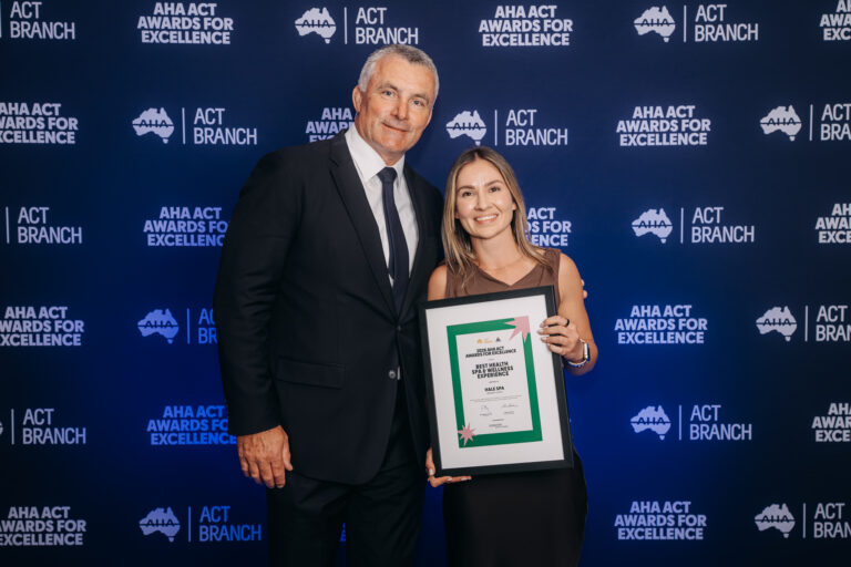 the award recipient photographed against the AHA ACT branded backdrop.