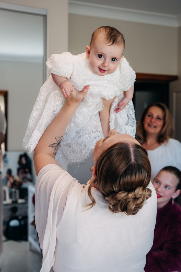 Mother lifting her baby during christening preparations at home