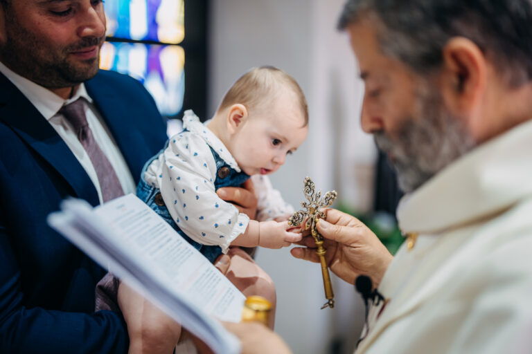 Baby reaching towards a cross during a Catholic christening ceremony