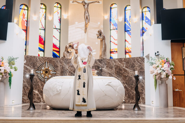 Catholic priest holding baby at the altar during a Sydney christening